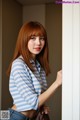 A woman in a blue and white striped shirt leaning against a wall.