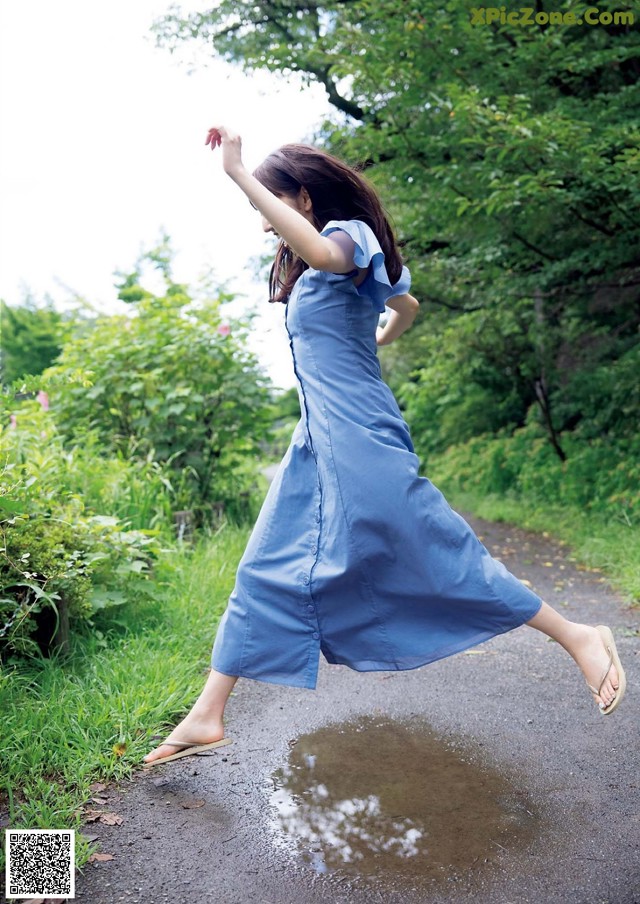 A woman in a blue dress is jumping in the air.