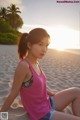 A woman in a pink tank top sitting on a beach.